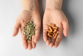 Female hands with plant based pills and dry herbs on white background