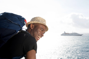 handsome young african american travel man smiling by the sea with cruise ship in background