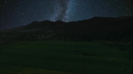 Wall Mural - aerial flight above field against mountains with milky way and stars on night sky