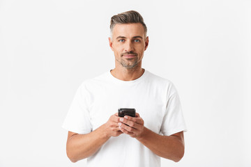 Wall Mural - Image of muscular man 30s wearing casual t-shirt holding and using smartphone