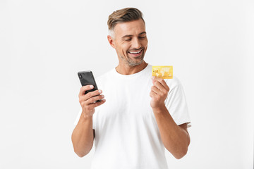 Wall Mural - Image of brunette man 30s wearing casual t-shirt holding smartphone and plastic credit card