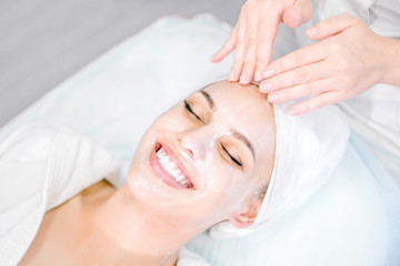 Beautician makes facial massage with mask. Beautiful smiling girl on spa procedure. Facial care.