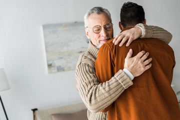 senior man in glasses smiling while hugging son