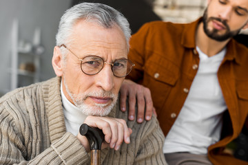 Wall Mural - cropped view of bearded son putting hand on shoulder of sad senior father in glasses