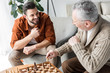 © LIGHTFIELD STUDIOS - retired father in glasses looking at happy son while playing chess