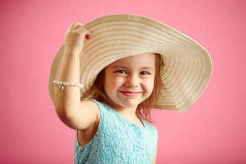 Wall Mural - Beautiful little girl in beach hat stands over pink isolated background.