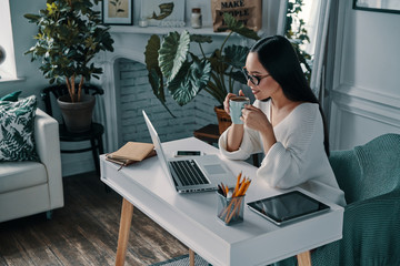 Planning another step. Top view of beautiful young woman working using computer and smiling while sitting in home office