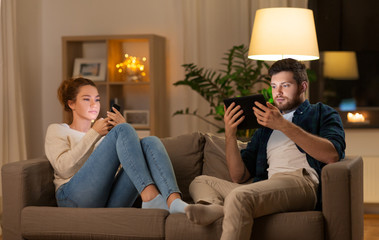 leisure, technology and internet addiction concept - couple with tablet computer and smartphone at home in evening