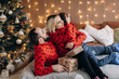 © kristina_1994 - Attractive parents and their little son in red sweaters have fun opening presents before a Christmas tree
