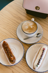 delicious sweet french eclairs and coffee in a coffee shop. Morning breakfast on a light table of a young girl. Coffee, handbag and two eclairs