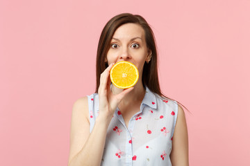 Excited young woman in summer clothes holding covering mouth with half of fresh ripe orange fruit isolated on pink pastel background. People vivid lifestyle relax vacation concept. Mock up copy space.