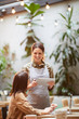 © Seventyfour - Cheerful pretty waitress in apron using tablet while talking to guest, businesswoman sitting at table with laptop and making order in coffee shop