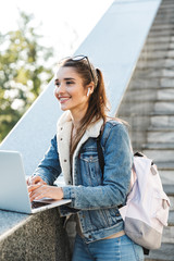 Sticker - Smiling young woman wearing jacket sitting on a bench