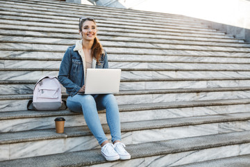 Canvas Print - Smiling young woman wearing jacket sitting on a bench