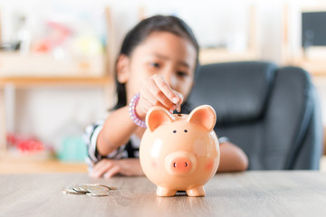 Asian little girl in putting coin in to piggy bank shallow depth of field select focus at the pig