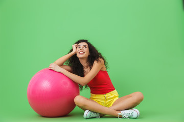 Wall Mural - Image of beautiful woman sitting on floor with fitness ball during aerobics against green wall