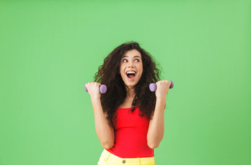 Wall Mural - Portrait of european girl doing sports and lifting weights against green wall