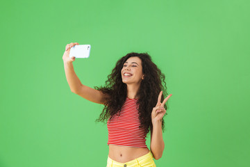 Canvas Print - Photo of content woman smiling and using cell phone for selfie isolated over green background