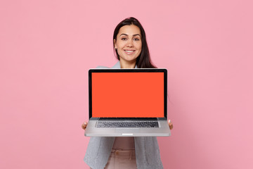 Portrait of smiling young woman in striped jacket holding laptop pc computer with blank empty screen isolated on pink pastel background. People sincere emotions, lifestyle concept. Mock up copy space.