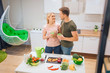 © estradaanton - Vegan loving couple holds detox drinks while cooking raw vegetables in the kitchen. Diet detox. Raw food diet. Happy family. Vegetarian food
