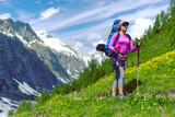 Fototapeta Las - Woman hiking in mountain range. Rear view of a female backpacker walking on a small foot path in a mountain landscape. Image for trekking, hiking or climbing.