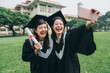 © PR Image Factory - two cheerful asian college girl study abroad standing outdoor on lawn finish bachelor degree. Capturing happy moments. happy female student in graduation gowns making selfie smiling hold smart phone