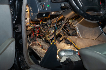 Poster - Automotive wiring under the wheel of an old German car, a disassembled dashboard for repairing and connecting electrical appliances with a portable lamp illuminating inaccessible places in a workshop