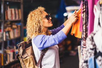 cheerful traveler young blonde curly woman looking and choosing clothes at the used market during al