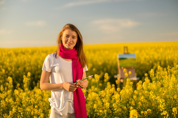 Wall Mural - girl painter with an easel in a yellow rapeseed field