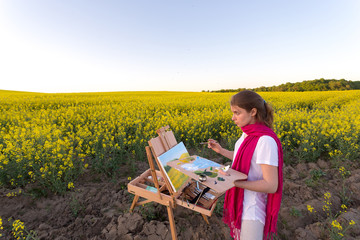 girl painter with an easel in a yellow rapeseed field