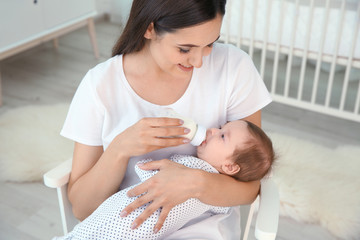 Wall Mural - Woman feeding her baby from bottle at home