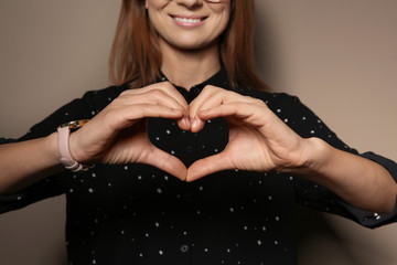 Wall Mural - Woman showing HEART gesture in sign language on color background, closeup