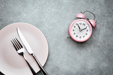 Alarm Clock And Plate With Cutlery. Concept Of Intermittent Fasting, Lunchtime, Diet And Weight Loss