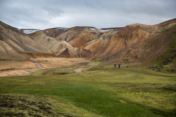 two tourists in the midst of a green valley among the colored Landmannalaugar mountains