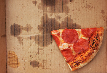 Pizza box with single slice of old pepperoni pizza in delivery box left after the party. Cold pizza leftovers in greasy cardboard, top view from above