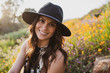 © Warren - Attractive young hispanic woman in a hat smiling while sitting in poppy fields at sunset