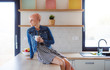 © Halfpoint - A young attractive woman sitting on a counter in a kitchen at home.