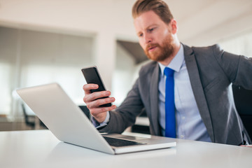 Wall Mural - Redhead entrepreneur using smart phone and laptop at work, low angle image.