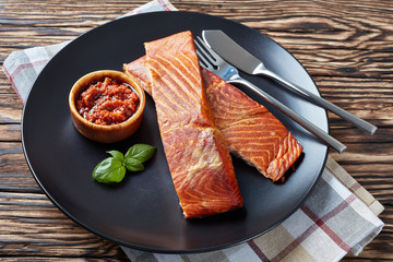 Wall Mural - baked salmon fillet on a black plate with sun dried tomatoes sauce on an old wooden table