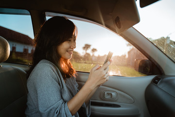 young asian woman using mobile phone while on passenger seat in the car