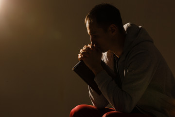 Poster - Religious young man praying to God on dark background, black and white effect
