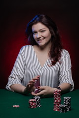 Brunette actress girl plays cards over green cloth posing on a dark background in blue and red light.