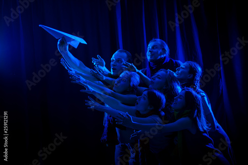 Canvastavla  The actors on the stage play a performance and look at a blue paper plane