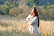 © CandyRetriever  - Selective focus medium shot of young beautiful asian women wearing vietnamese hat standing and smiling in golden and green wheat field in the morning sunny day with blurred forest backgrounds.