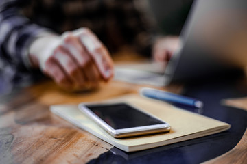 Close-up image of male hand using smartphone at modern interior of street urban cafe shop, searching or social networks concept, hipster man typing an sms message to his friends