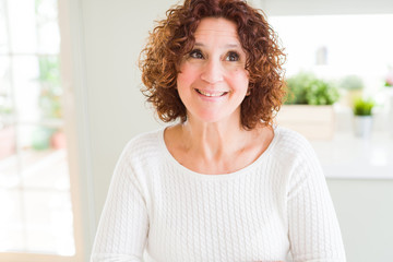 Beautiful senior woman wearing white sweater at home smiling looking side and staring away thinking.