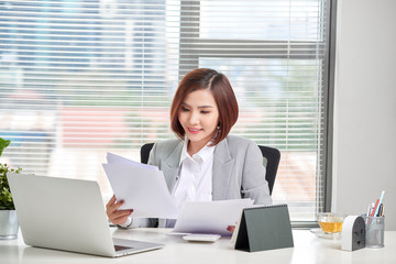 Sticker - Happy asian woman working in office. Female going through some paperwork at work place.