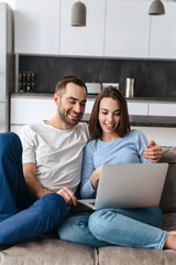 Poster - Image of satisfied couple using laptop together while sitting on sofa in living room at home