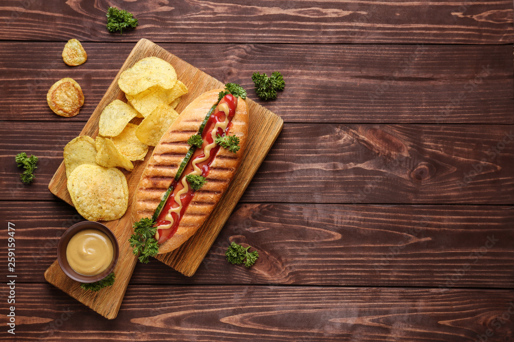 Board with tasty hot dog on wooden background