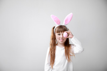 Poster - Cute little girl with Easter egg and bunny ears on light background